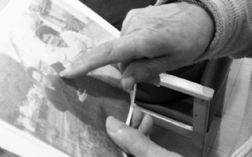 Mano de una persona mayor señalando una foto antigua.