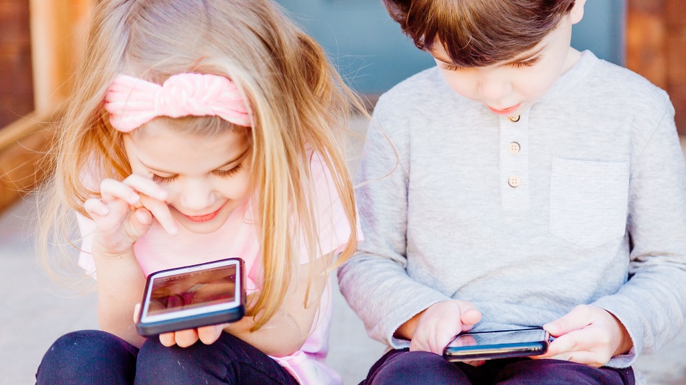 Dos niños usando su respectivo móvil.