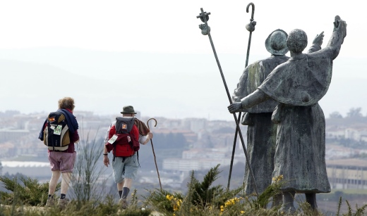 Peregrinos en Santiago de Compostela pasando al lado de una estatua que representa a peregrinos.