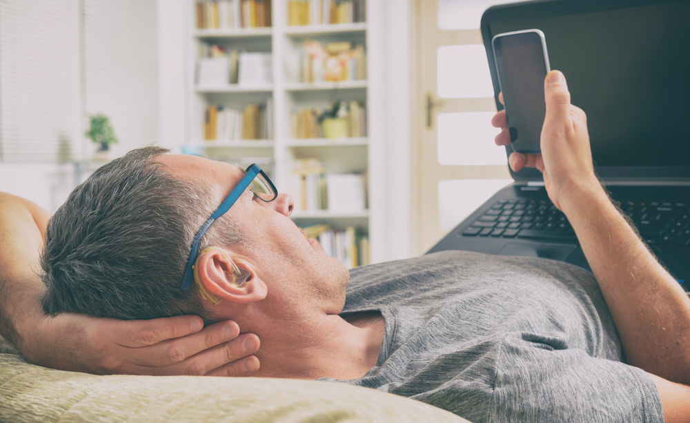 Un home con audífono utiliza o seu smartphone e o seu computador portátil.