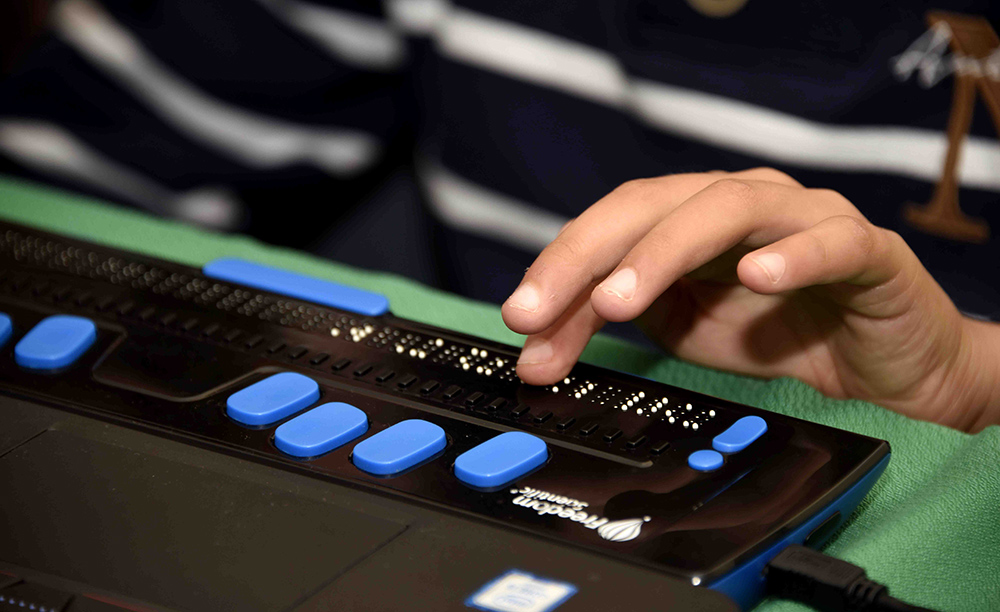 Unha persoa utiliza unha liña braille conectada a un computador.