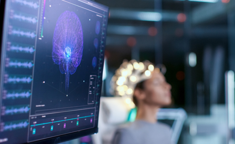 Imaxe dunha pantalla mostrando sinais cerebrais dunha muller sentada ao fondo.