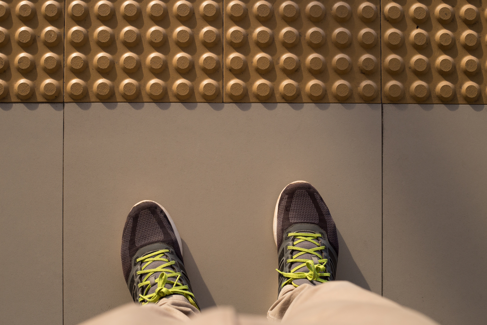 Una persona parada al lado de las guías para personas ciegas de una acera.