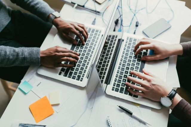 Vista cenital de una mesa de trabajo donde hay dos portáiles contrapuestos en los que está trabajando dos personas.