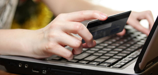 Mano sosteniendo una tarjeta de crédito por encima de un portátil.