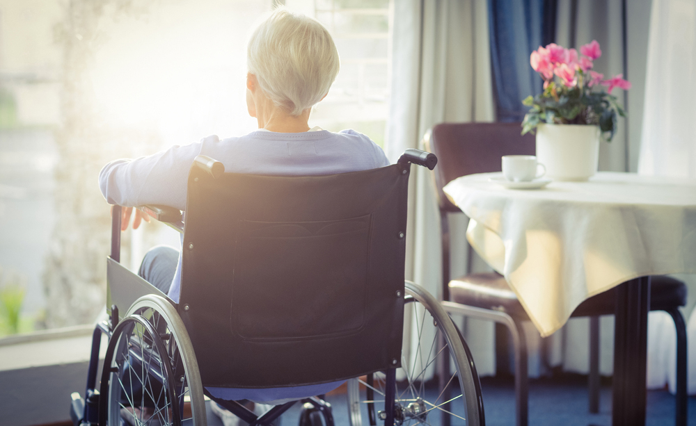 Una mujer con ELA mira a través de la ventana de su casa.
