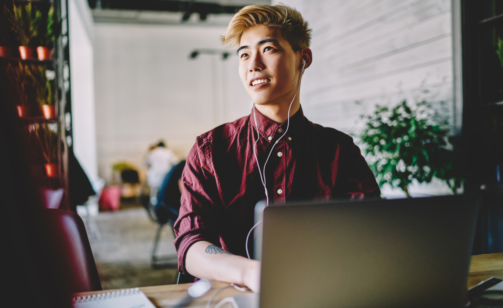 Un mozo utiliza o seu computador portátil cuns auriculares.