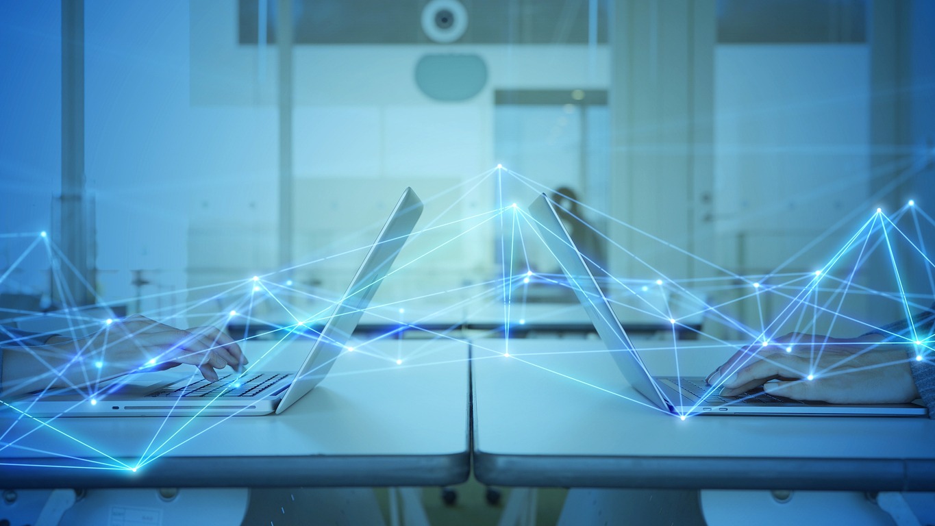 Manos tecleando en dos portátiles.