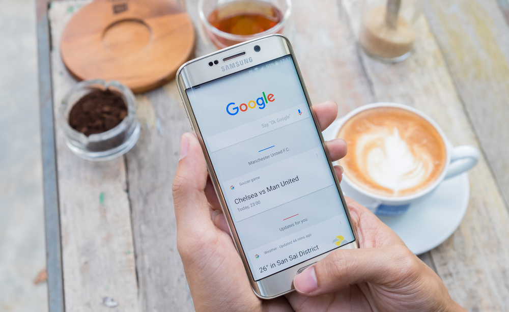 Una personas sujeta un teléfono móvil encima de una mesa en la que hay un café.