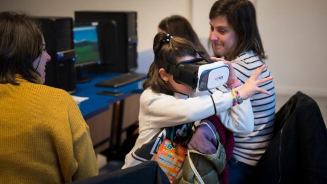 Una niña, entre dos mujeres, usando gafas de realidad virtual.