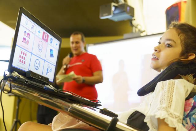 Niña en cadera de ruedas usando una tablet que muestra pictograma.