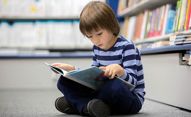 Un niño lee un cuento sentado en el suelo de una biblioteca.