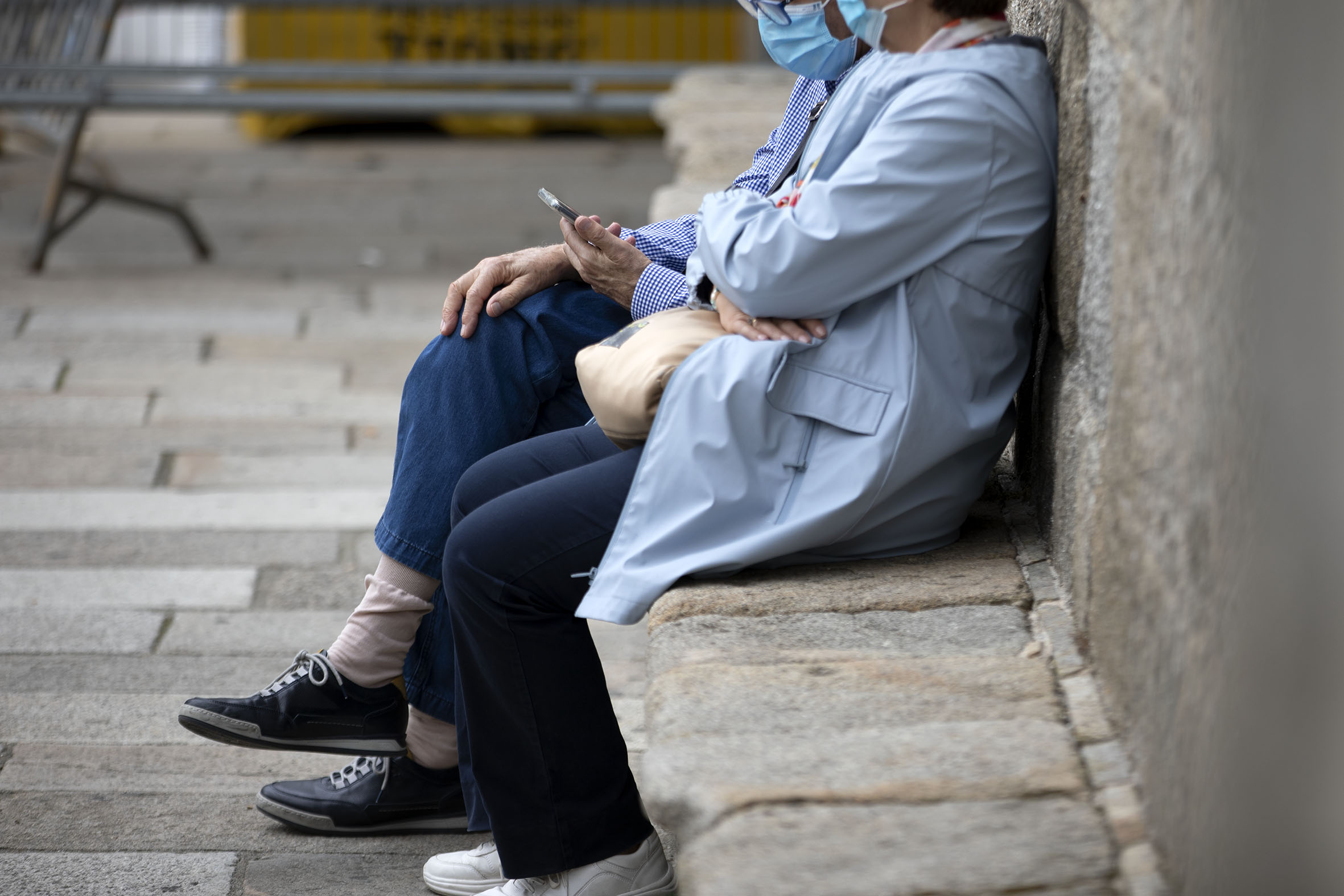 Dos personas mayores sentadas en la calle usando un smartphone.