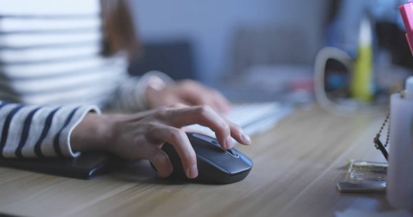 Mano usando un ratón delante de una pantalla.