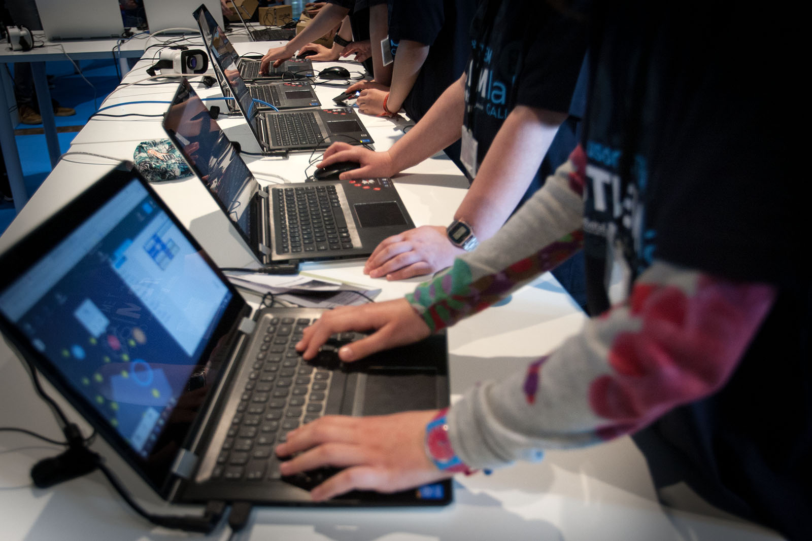 Varios mozos de pé diante de cadanseu portátil que están enriba dunha mesa.