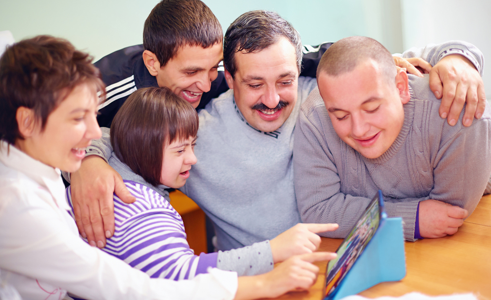 Varias personas con discapacidad miran y se divierten utilizando una tableta.