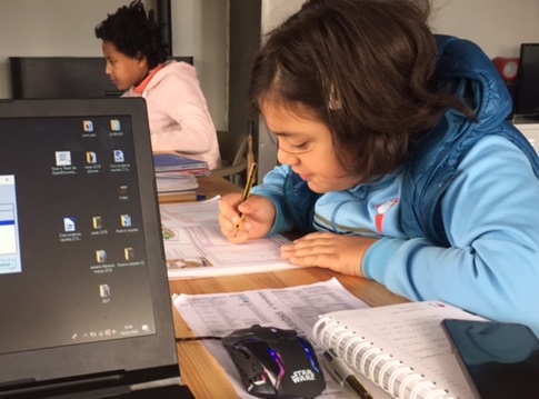 Niñas en un aula resolviendo ejercicios con un portátil en primer plano.