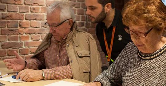 Dúas persoas maiores usando dispositivos móbiles asesorados por un mozo.