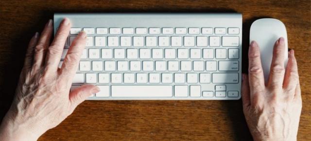 Manos de persona mayor sobre un teclado y un ratón.