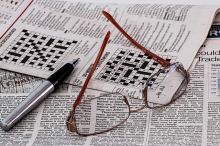 Unhas lentes e un bolígrafo encima dun xornal que mostra crucigramas.