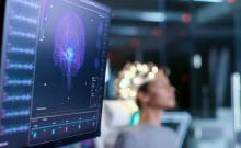 Imagen de una pantalla mostrando señales cerebrales de una mujer sentada al fondo.