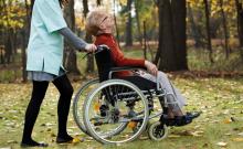 Una mujer cuida de una mujer mayor en silla de ruedas en un parque.