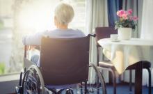 Una mujer con ELA mira a través de la ventana de su casa.