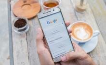 Una personas sujeta un teléfono móvil encima de una mesa en la que hay un café.