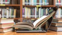 Libro abierto encima de un portátil en una biblioteca.