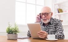 Un home maior utiliza unha tableta mentres fala por teléfono.