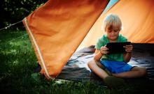 Un niño utiliza una tableta en una tienda de campaña en el campo.