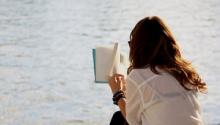 Mujer de espaldas leyendo un libro.