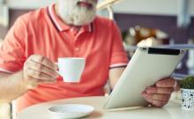 Un home maior utiliza unha tableta mentres toma un café.