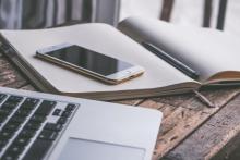 Un portátil, un smartphone y una agenda de papel arriba de una mesa.