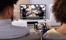 Dos jóvenes ven la televisión en el televisor y en un móvil.