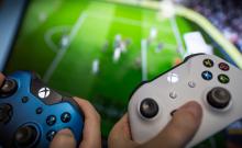 Dos jóvenes sujetan sendos mandos de la Xbox One delante de un televisor.